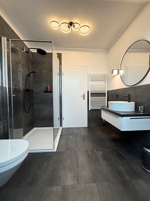 Une salle de bain moderne avec une douche à parois de verre, des toilettes blanches, un lavabo avec un miroir et un porte-serviettes.