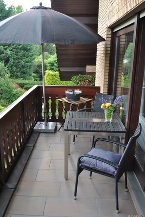 Un balcon avec une table et des chaises, une plante en pot et un grand parasol.