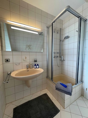 Enjoy a refreshing shower or soak in the bathtub in this bathroom, featuring a corner sink and glass-enclosed shower.
