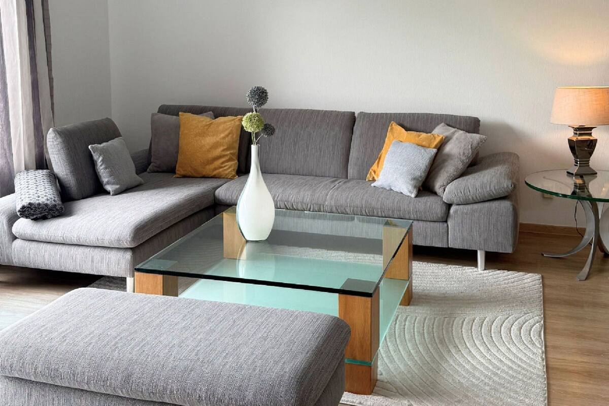 A modern living room with a sectional sofa, a glass coffee table, and a small side table with a lamp.