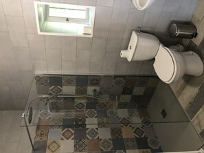 A modern bathroom with a glass-enclosed shower, patterned tiles, a toilet, and a small window.