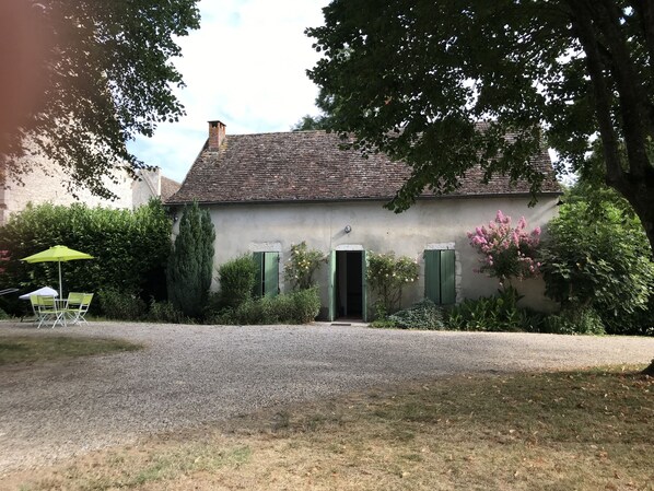 A rustic stone building with a gravel driveway, a green umbrella, and a chair.