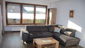 A living room with a sectional sofa, a wooden coffee table, and a large window with a view of the outside. - Ferienwohnung Friedrich (Schonungen)