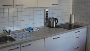 A kitchen with white cabinets, a stainless steel sink, a kettle, and a roll of paper towels. - Ferienwohnung Friedrich (Schonungen)