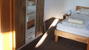 A bedroom with a wooden bed, a nightstand, a mirror, and a wardrobe. - Ferienwohnung Friedrich (Schonungen)