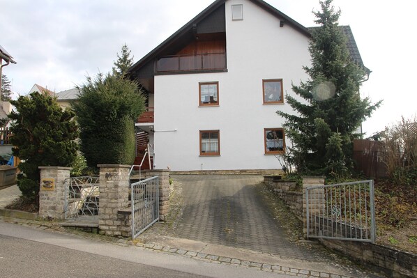 A two-story house with a white exterior, a sloped roof, and a front entrance with a metal gate. - Ferienwohnung Friedrich (Schonungen)