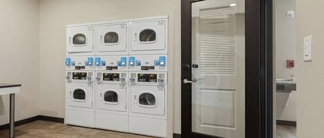 A laundry area with multiple washing machines and dryers, a door with a fire alarm, and a small table.