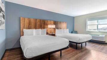A hotel room with two beds, a wooden headboard, a nightstand, a lamp, and a window with a view.