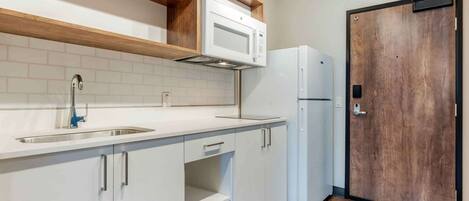 A kitchen with white cabinets, a stainless steel sink, a microwave, and a refrigerator.