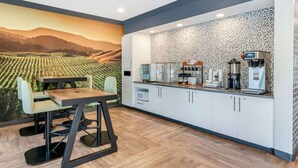 A modern kitchen with white cabinets, a countertop with coffee machines, and a mural of a vineyard. - Extended Stay America Premier Suites Ukiah (Ukiah)