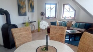Una sala acogedora con una mesa redonda, sillas de mimbre, un sofá y un calentador negro.
