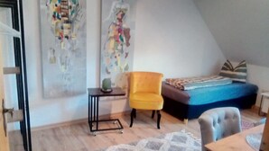 Una habitación con una cama, un sillón amarillo, una mesita y una alfombra estampada.