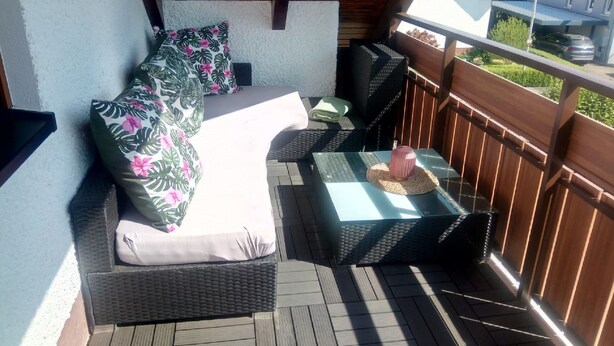 Un balcón con cama, mobiliario de mimbre y vista al barrio.