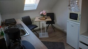 Una cocina compacta con estufa, lavamanos, microondas y un refrigerador pequeño. Hay una mesa de comedor con sillas y un florero con flores.