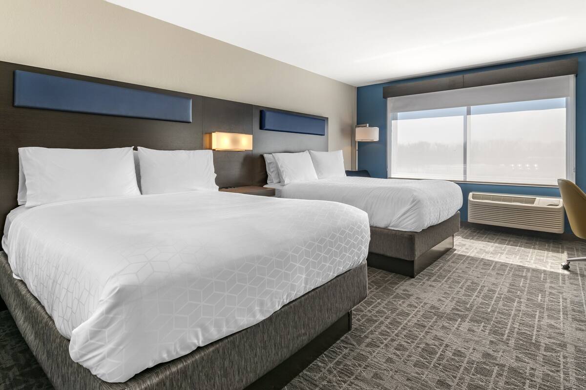 A hotel room with two beds, a large window, and a view of the city skyline.