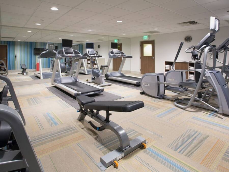 A gym with various exercise machines, including treadmills and elliptical trainers, arranged on a carpeted floor.