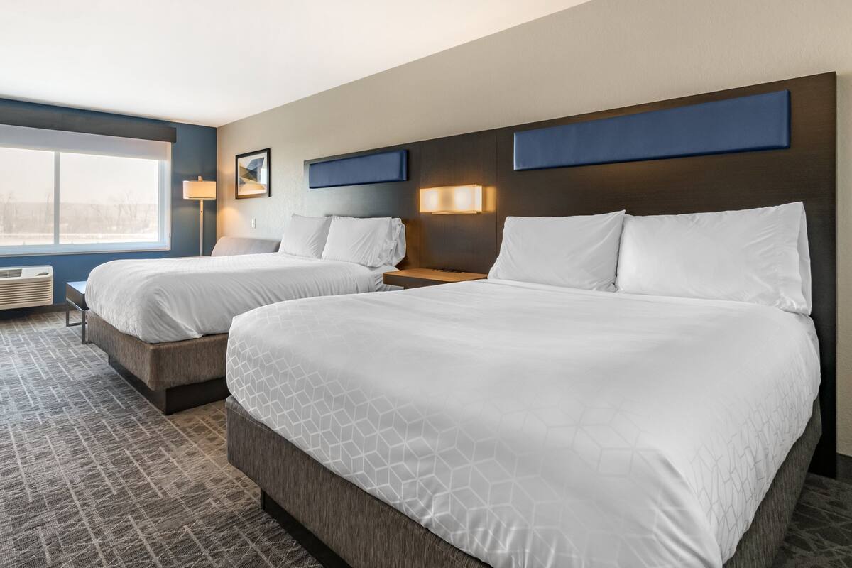 A hotel room with two beds, a large window, and a wall-mounted lamp.