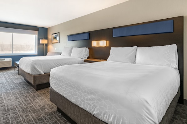 A hotel room with two beds, a large window, and a wall-mounted lamp.