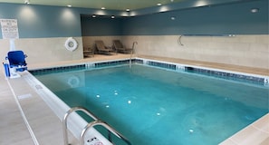An indoor swimming pool with a lifeguard chair, lounge chairs, and a warning sign.