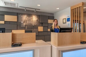 Zona de recepción con diseño moderno, que incluye un mostrador de madera, una pantalla digital y un letrero en la pared para Holiday Inn Express & Suites.