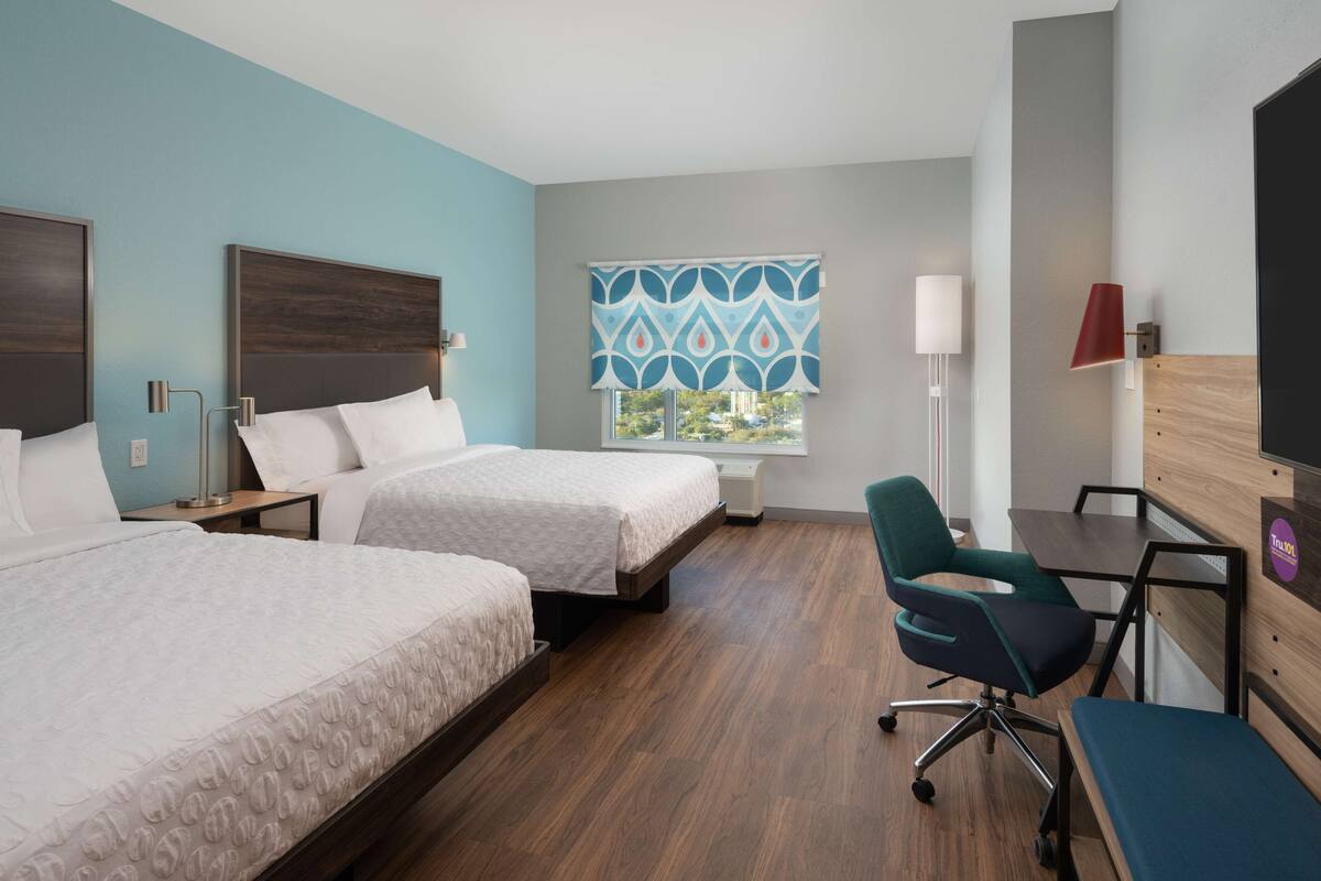 A hotel room with two beds, a desk, a chair, a TV, and a window with a view.