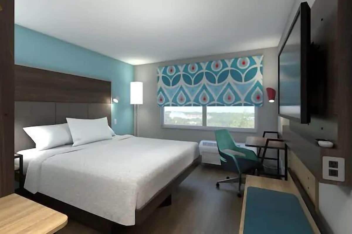 A hotel room with a bed, a desk, a chair, a TV, and a window with a view.