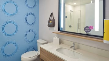 A bathroom with a blue wall, a white toilet, a wooden vanity with a sink, and a mirror.