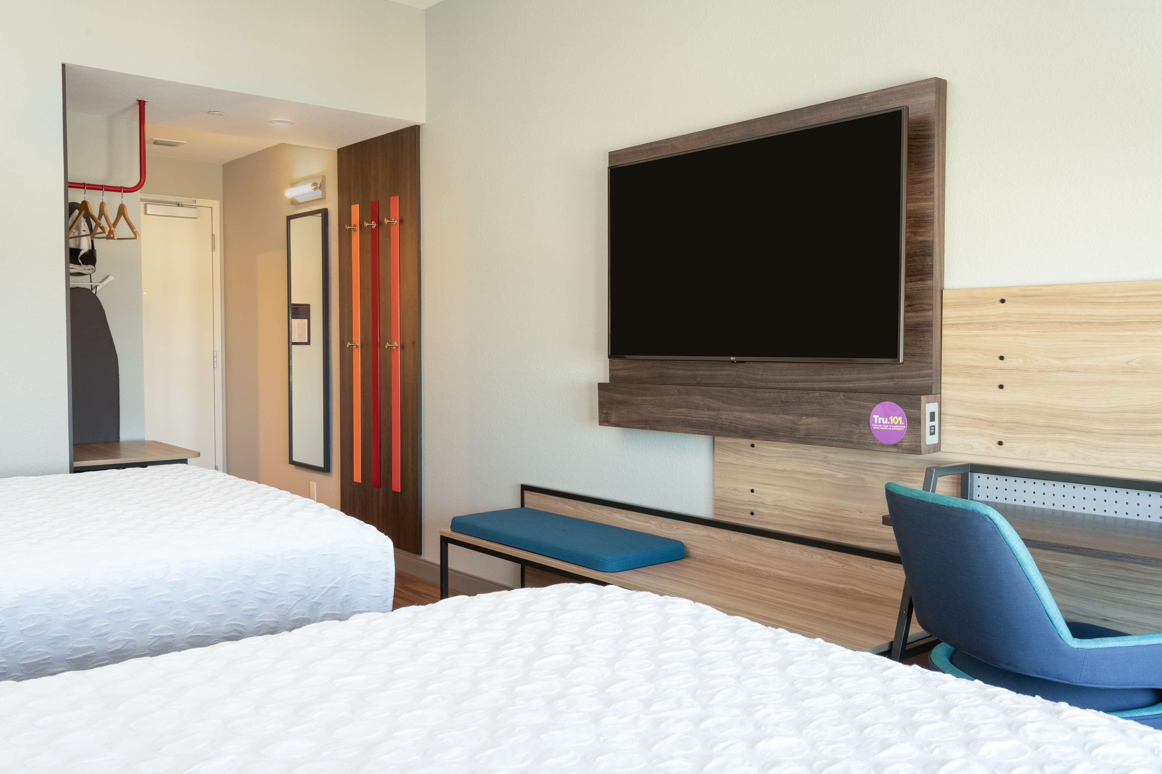 A hotel room with two beds, a desk with a chair, a TV mounted on the wall, and a door leading to a bathroom.