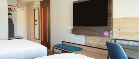 A hotel room with two beds, a desk with a chair, a TV mounted on the wall, and a door leading to a bathroom.