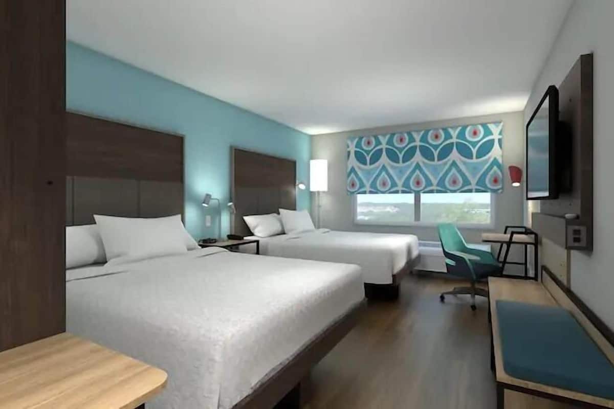 A hotel room with two beds, a desk, a chair, a TV, and a window with a view.