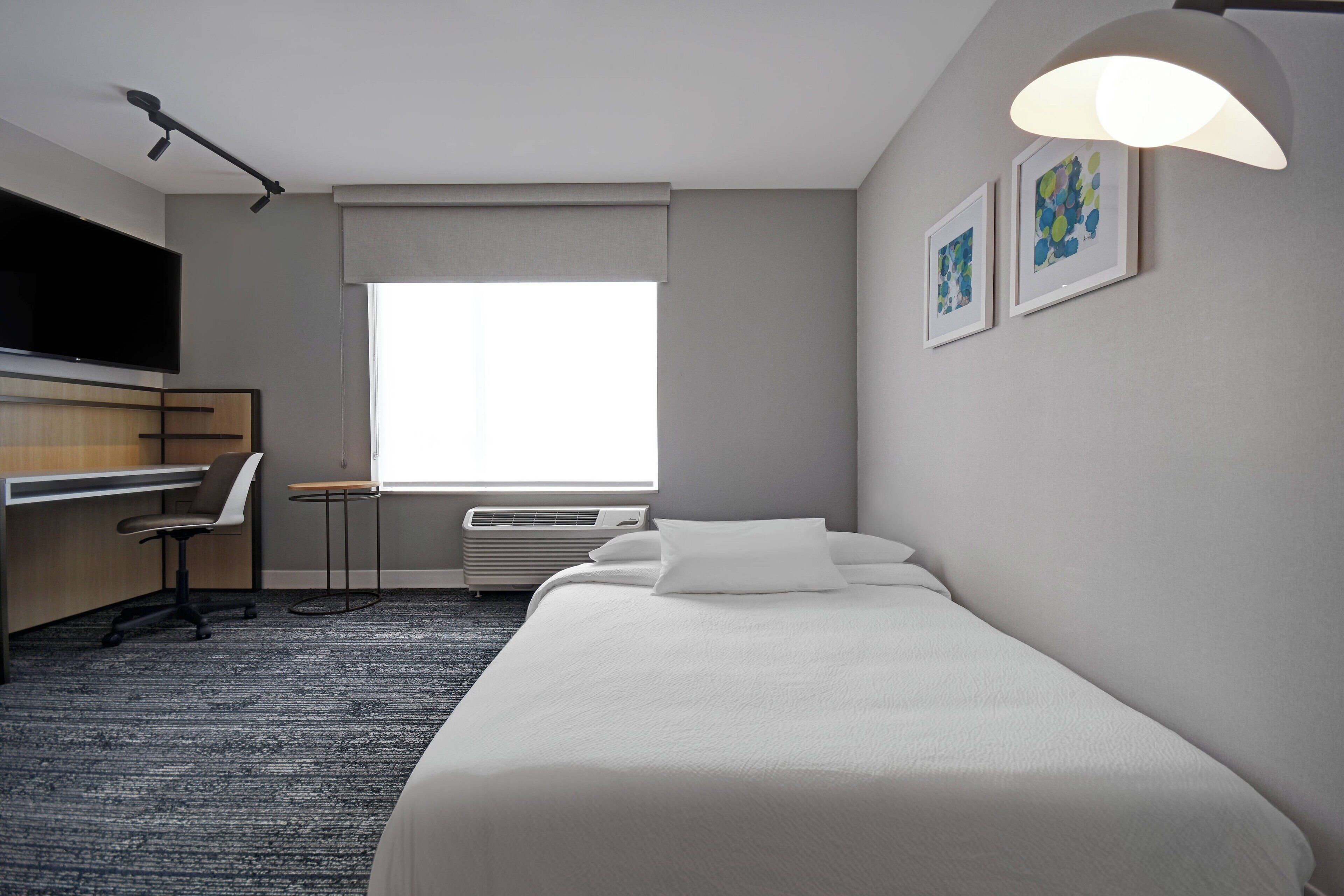 Une chambre d’hôtel équipée d’un lit, d’un bureau, d’une chaise, d’une télévision et d’une fenêtre donnant sur un paysage agréable.