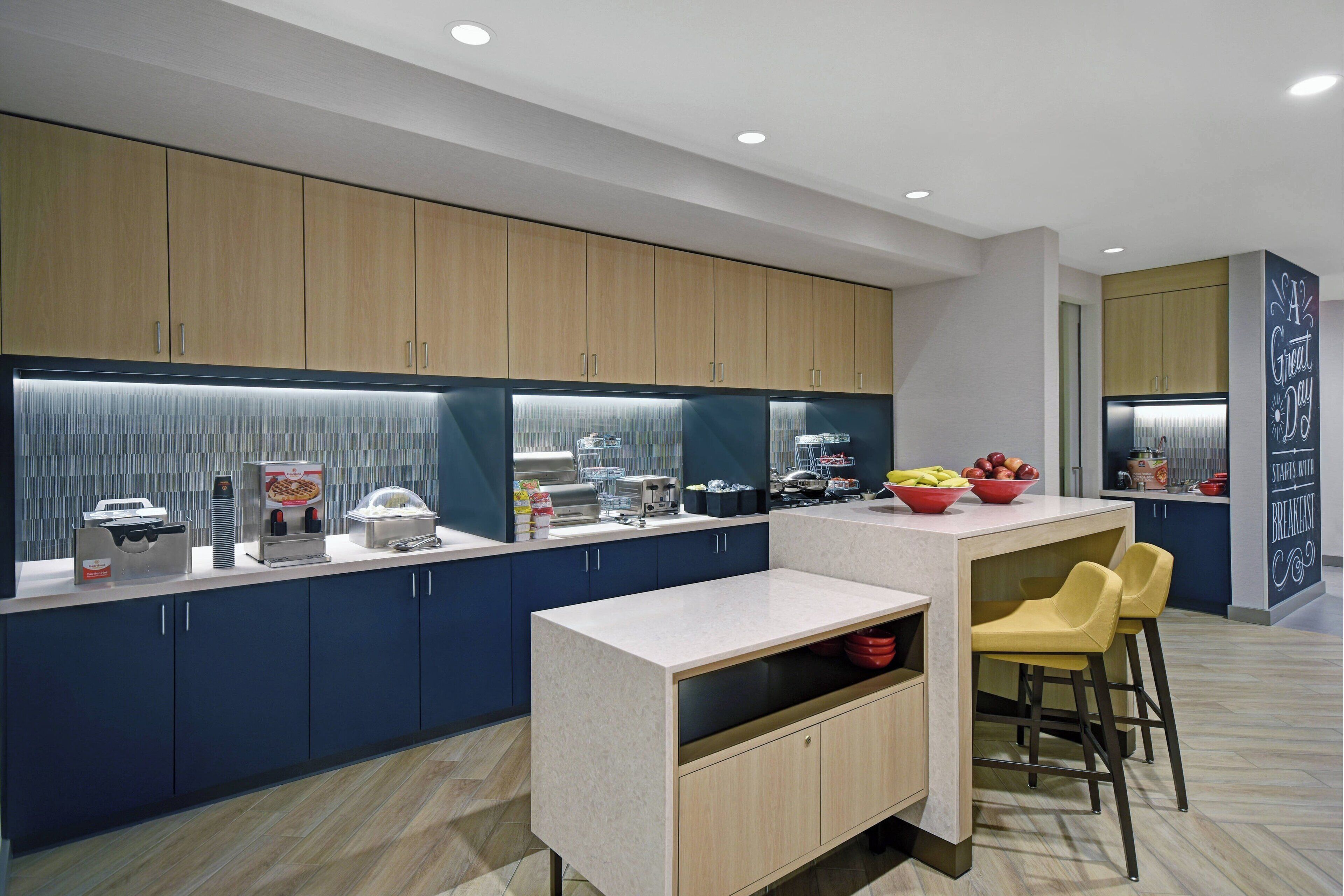 A modern kitchen with dark blue cabinets, a light countertop, and a built-in island with bar stools.