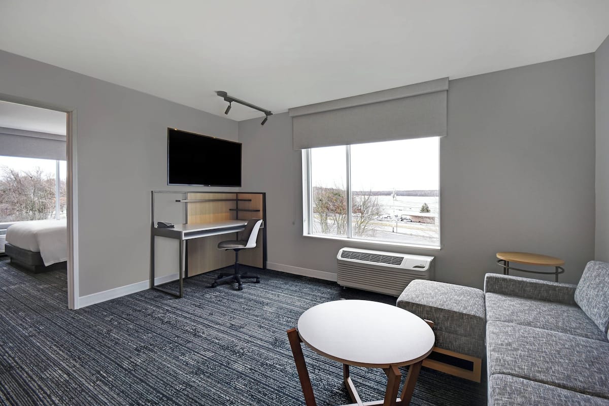 A modern hotel room with a bed, desk, chair, and a large window offering a view.