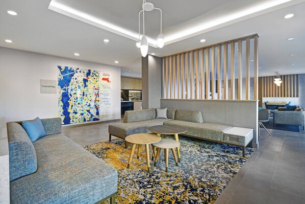 A modern lobby with a sectional sofa, round tables, and a colorful abstract wall art.