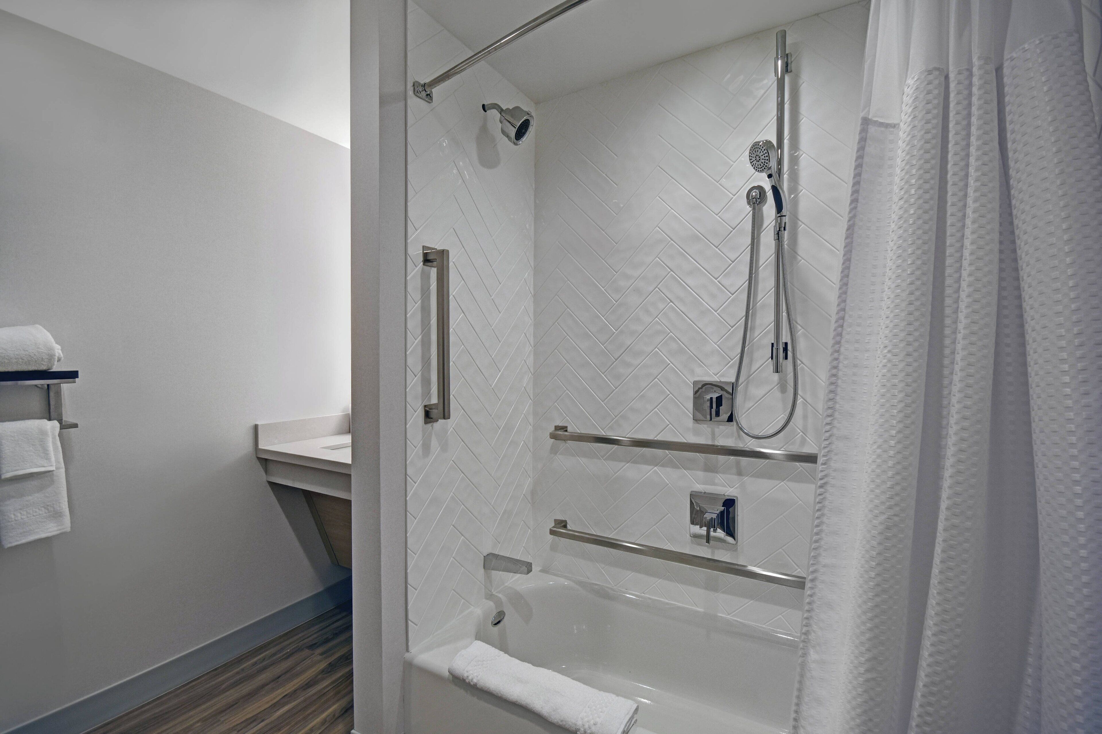 Un baño moderno con ducha de vidrio, bañera y tocador con toallero.