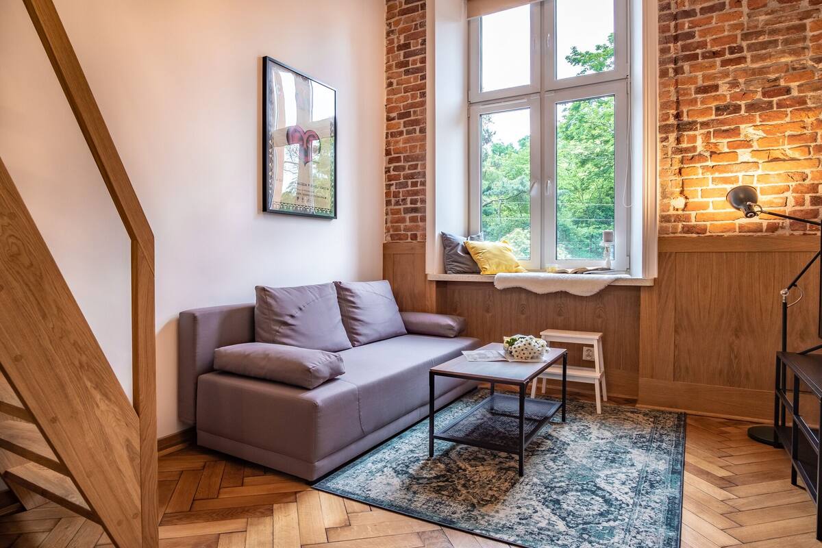 Un salon moderne avec un canapé gris, une petite table basse et une fenêtre donnant sur un paysage verdoyant.