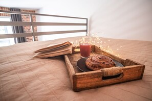 A wooden tray with a pastry, a glass of red drink, and a book on a bed with a striped headboard.