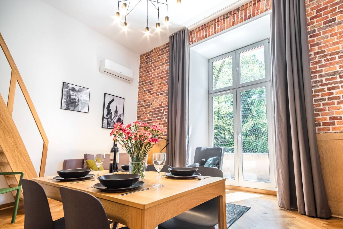 Un coin repas avec une table en bois, des assiettes noires et un vase de fleurs.