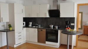 A compact kitchen with white cabinets, a black countertop, a dishwasher, an oven, and a small round table with fruits. - Ferienwohnung Gäste Oase (Bad Windsheim)