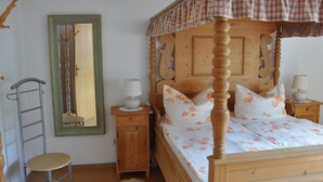 A four-poster bed with floral bedding, a wooden nightstand with a lamp, a wooden wardrobe, and a mirror on the wall. - Ferienwohnung Gäste Oase (Bad Windsheim)