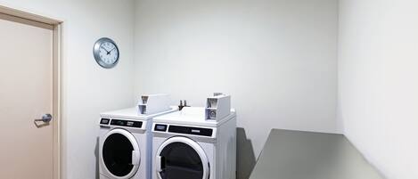 Un lavadero con dos lavadoras de carga frontal, un reloj en la pared y una pequeña mesa.