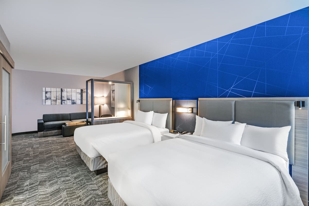 A hotel room with two beds, a sofa, a mirror, and a blue accent wall.