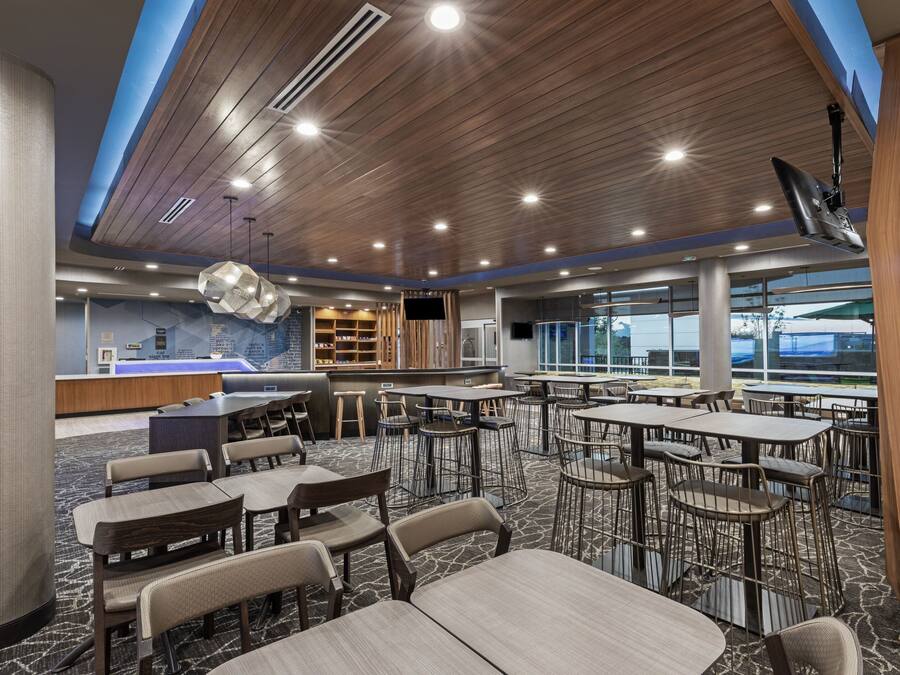 A spacious dining area with multiple tables and chairs, a reception desk, and a large window providing a view of the outdoors.
