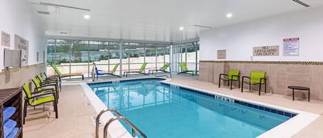 Una piscina interior con señalización de seguridad clara, varias zonas de estar y vistas al exterior.