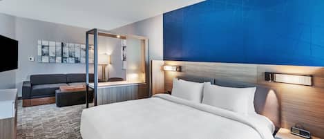 A hotel room with a large bed, a sofa, a desk, and a TV.