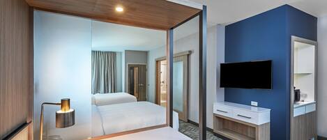 A hotel room with a bed, bedside table, lamp, TV, and a mirror.