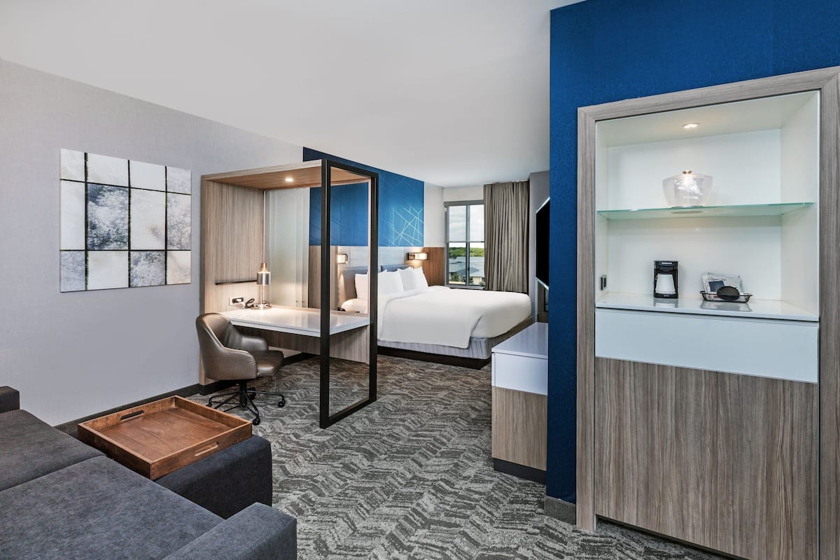 A hotel room with a bed, desk, chair, and a small wooden tray table.