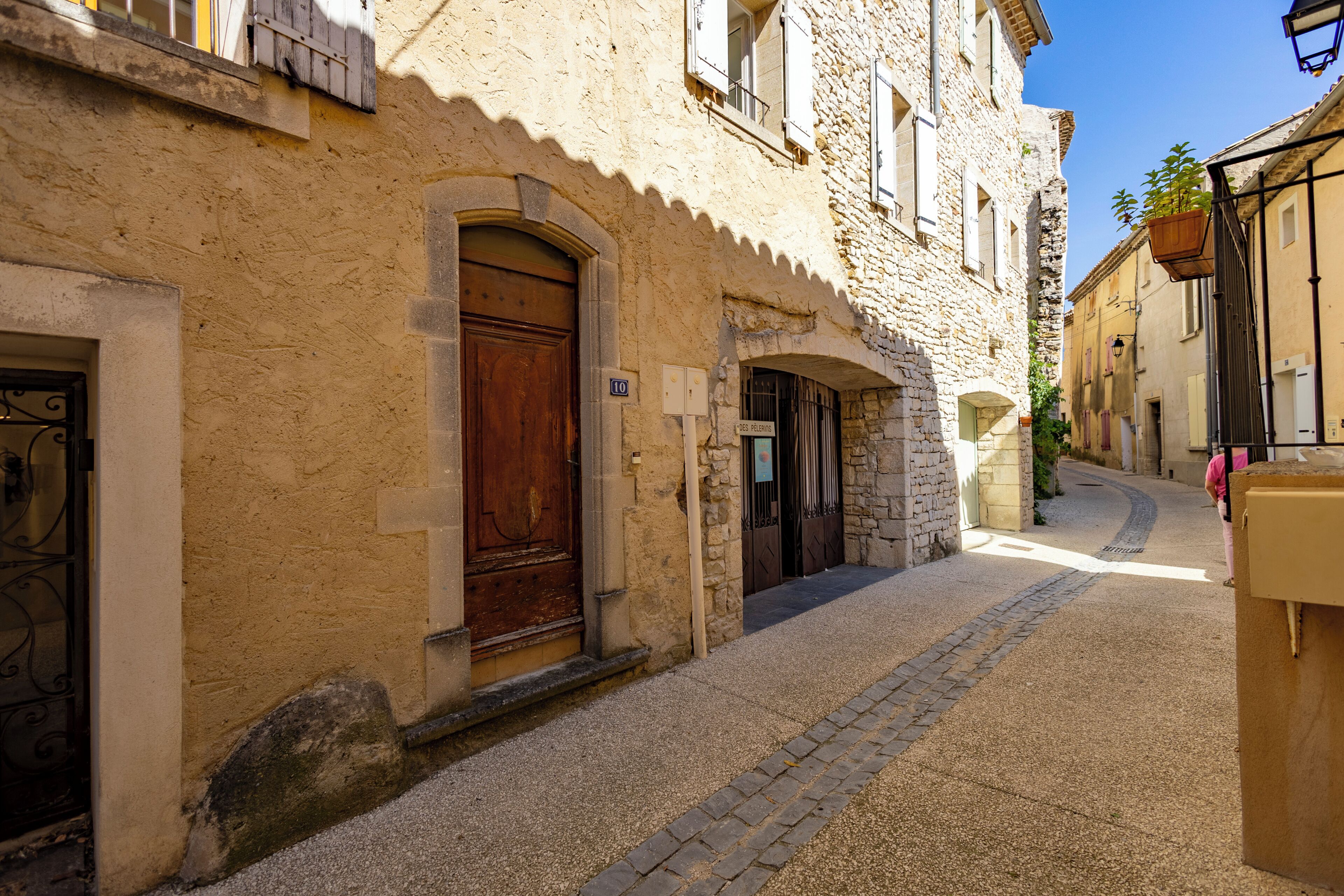 Una estrecha calle adoquinada con edificios históricos de piedra, una puerta de madera y una planta colgante.