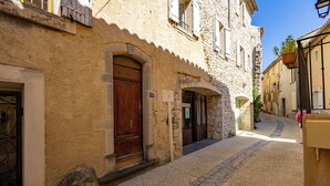 A narrow cobblestone street with historic stone buildings, a wooden door, and a hanging plant. - La Baume des Pèlerins (Sablet)