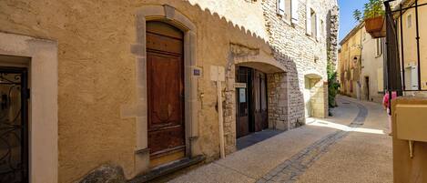 Una estrecha calle adoquinada con edificios históricos de piedra, una puerta de madera y una planta colgante.